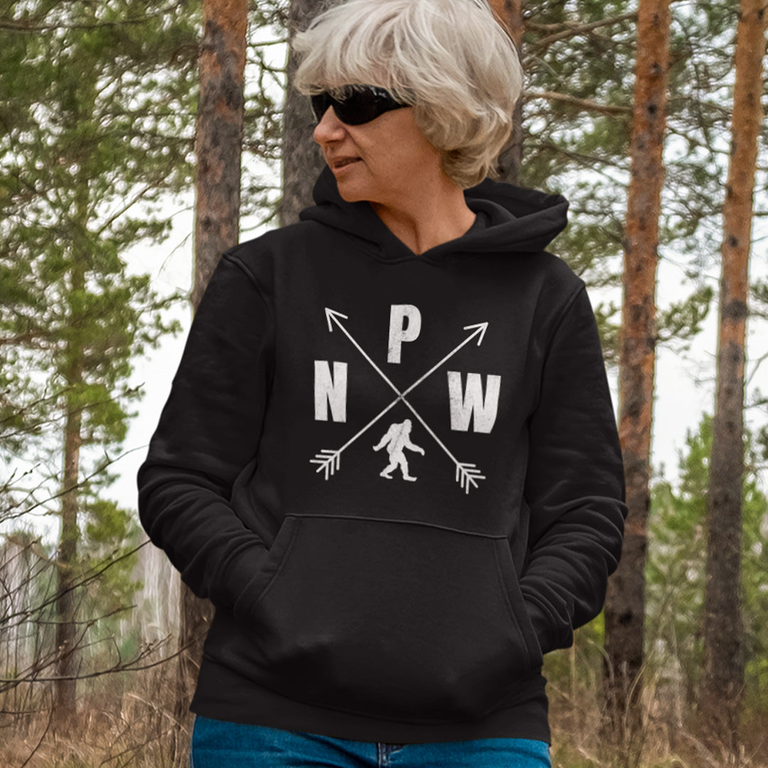 Woman wearing a black PNW crossed arrows compass design Bigfoot hoodie